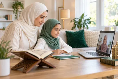 A mother in an ivory hijab and her young daughter, both attentive to a female teacher on a laptop in a calm home study with Quran learning materials